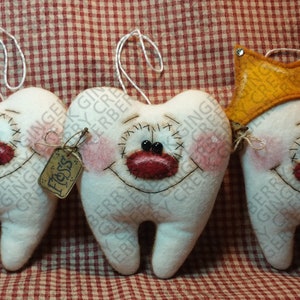 May include: Three handmade tooth-shaped ornaments with smiling faces, blush, and red lips. One has a pink bow, another a tag that says "Floss", and the third a yellow crown. Each has a string for hanging.