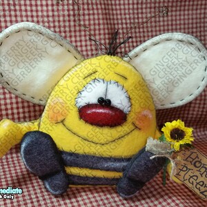 May include: A handmade yellow and black bee-shaped plushie with large white wings, holding a sunflower and a tag that says "Honey Pleez". The bee has a smiling face with a red mouth and is set against a red and white checkered background.