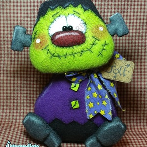 May include: A handmade Frankenstein's monster doll with a green head, black hair, and a stitched smile. The doll has a purple body, gray feet, and a blue scarf with yellow stars. A tag reads "Jolt".