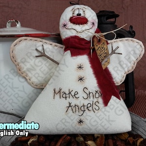 May include: A handcrafted snowman angel doll with embroidered details. The doll features a white body, a red scarf, and twig arms. The words "Make Snow Angels" are stitched on the front. A tag reads "Snow Flak".