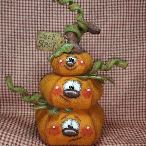 May include: A stacked pumpkin decoration with three orange pumpkins, each with a smiling face, rosy cheeks, and white eyes. Green vines and a brown stem top the pumpkins. A small tag reads "Jack Stack".
