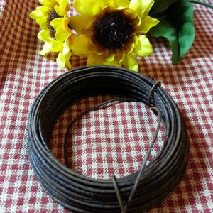May include: A coil of dark brown floral wire sits on a red and white checkered surface, with bright yellow sunflowers in the background. The wire is tightly wound, and a loose end extends from the coil.