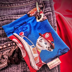 May include: A blue and red fabric pouch with a cartoon image of a dog in a police car. The pouch has a metal clip and a tag that reads "Handmade in USA, NecoCreations.com".