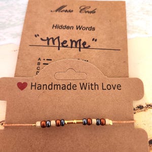 May include: A handmade Morse code bracelet with the word "Meme" spelled out in beads. The bracelet is displayed on a brown card that reads "Handmade With Love" and "Best Wishes."