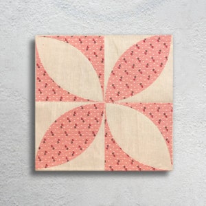 Puede incluir: Un bloque de colcha rosa y blanco con un dise&ntilde;o geom&eacute;trico. El bloque est&aacute; hecho de tela con un peque&ntilde;o patr&oacute;n floral rojo y blanco.