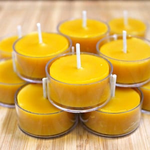 Może przedstawiać: Grupa żółtych świeczek typu tealight w przezroczystych szklanych pojemnikach. Świece są ułożone w kształt piramidy na drewnianej powierzchni.