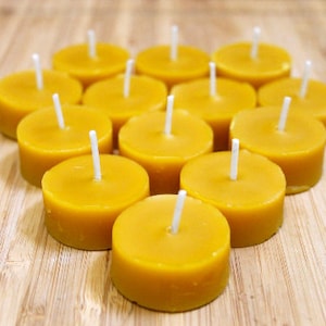 May include: A group of 12 yellow tea light candles arranged in a heart shape on a wooden surface.