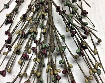 May include: A close-up of a decorative twig spray with teardrop-shaped berries. The berries are in shades of burgundy, green, and yellow. The twigs are brown and wrapped together at the base.