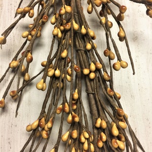 May include: Close-up of a decorative floral stem with brown stems and teardrop-shaped berries. The berries are a mix of light and dark yellow, with a glossy finish. The stems are wrapped in brown paper.