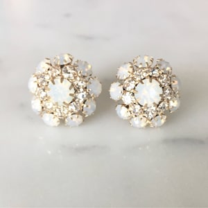 Puede incluir: Un par de pendientes de tono dorado con piedras de ópalo blanco. Los pendientes son redondos y tienen un grupo de piedras en el centro.