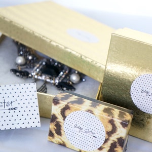 May include: Three gold boxes with the text "Edgy Sister" on them. One box has a leopard print design, one has a white background with black polka dots, and one has a black and white necklace inside.