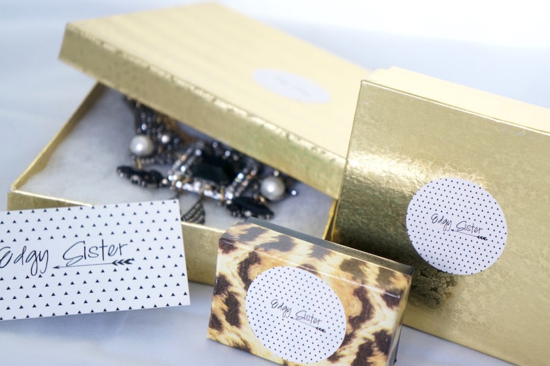 May include: Three gold boxes with the text "Edgy Sister" on them. One box has a leopard print design, one has a white background with black polka dots, and one has a black and white necklace inside.