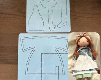 May include: Two light blue stencils with doll patterns and a finished doll. The stencils have dotted lines for cutting out doll parts. The doll has brown braids, a blue floral dress, a white apron, and green shorts. The doll is approximately 10 inches tall.