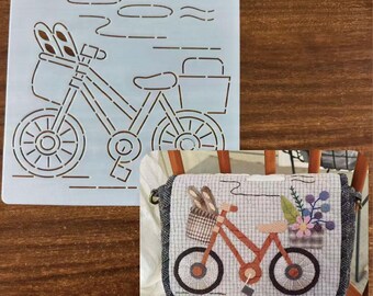 May include: A light blue stencil featuring a bicycle with a basket holding baguettes and a rear basket. A small, decorative bag with a bicycle design, flowers, and baguettes is also visible.