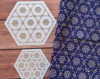 May include: Two light-colored, hexagon-shaped wooden coasters with a geometric floral design. A navy blue fabric with a white floral pattern is next to the coasters. The coasters and fabric are on a wooden surface.