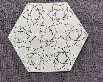 May include: A white, hexagon-shaped decorative tile with a repeating pattern of interlocking, black, dashed-line floral designs. The tile is set against a textured, gray background.