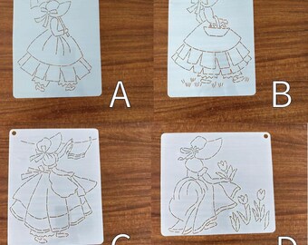 May include: Four light blue stencils with vintage lady designs. Each stencil features a different pose of a woman in a dress and hat. One holds an umbrella, another a basket, a third a handkerchief, and the last, flowers. Each stencil has a small hole at the top.