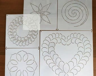 May include: A collection of white quilting stencils featuring various designs, including a flower, spiral, wreath, heart, and floral pattern. Each stencil is square and has small holes in the corners for alignment. The stencils are designed for fabric art and quilting projects.