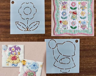 May include: A collection of craft stencils and a small quilt. The stencils are light blue and feature a flower, a girl holding a balloon, and a quilt pattern. The quilt is square, with a green and pink border, and features teddy bears and flowers.