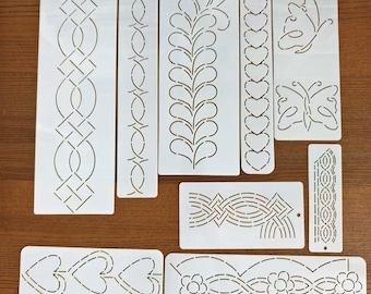 May include: A collection of white plastic stencils with various decorative designs, including geometric patterns, hearts, butterflies, and floral motifs. The stencils are arranged on a wooden surface, offering a variety of creative options for crafts and art projects.
