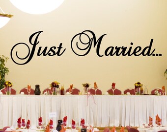 May include: A wedding reception venue with white tablecloths and red napkins. The head table has a sign that reads "Just Married..."
