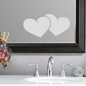 May include: Two white heart-shaped decals on a mirror above a bathroom sink with two chrome faucets.