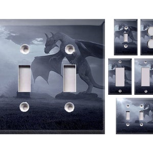 May include: A set of light switch covers featuring a fantasy illustration of a dragon in a dark, misty landscape. The dragon is gray and has wings spread wide. The background is a dark blue with hints of purple and white clouds.