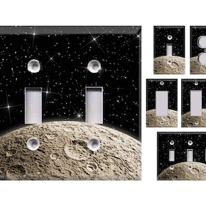 May include: Decorative light switch covers featuring a space-themed design. The covers showcase a detailed moon surface against a starry black background. Various configurations include single, double, and triple switch plates, and an outlet cover.