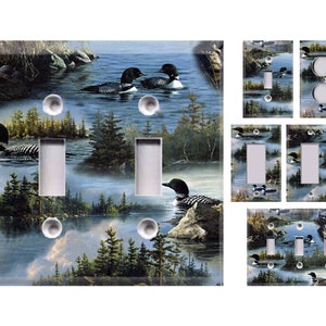 May include: A set of light switch and outlet covers featuring a scenic lake scene with loon birds. The covers are printed with a watercolor-style image of a lake, trees, and loons.