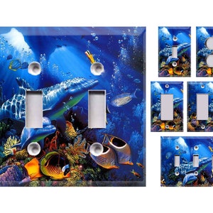 May include: Decorative light switch covers featuring an underwater scene with dolphins, colorful fish, and coral reefs. The covers are primarily blue with a glossy finish. Various configurations are shown, including single and double switch plates, and outlet covers.