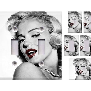 May include: A set of light switch covers featuring a black and white image of Marilyn Monroe. The covers are white with a glossy finish. The image is cropped to show Monroe's face and shoulders. The covers are designed to fit standard light switches.