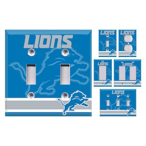 May include: A set of six light switch covers featuring the Detroit Lions logo. The covers are blue with a white and gray stripe. The logo is a silver lion with the word "Lions" in silver lettering.