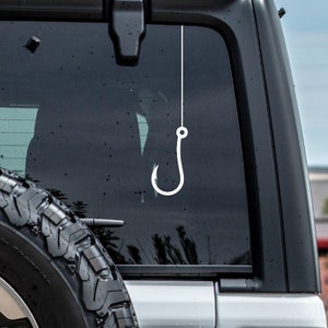 May include: A white fishing hook decal hanging from the rear window of a black car.