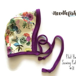 May include: A purple and white floral pilot hat sewing pattern. The pattern is called "Pilot Hat Sewing Pattern #31" and is from the company "Needlefish".