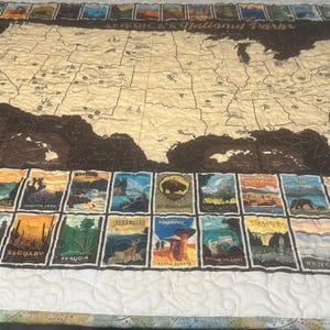 May include: A quilted map of the United States with a brown outline and beige interior. The map is surrounded by colorful rectangular images of national parks. The quilt has a white border.