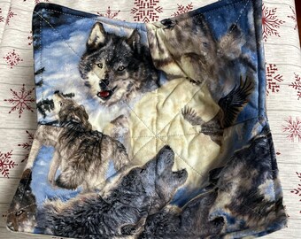 Puede incluir: Un salvabols cuadrados con un diseño de manada de lobos. La tela representa lobos aullando a la luna, con una escena invernal azul y blanca. El salvabols está acolchado y tiene un borde cosido.
