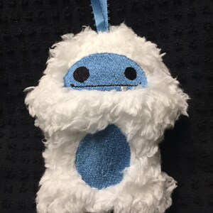 Puede incluir: Adorno de yeti de peluche blanco con cara y vientre azules. El yeti tiene ojos bordados negros y boca cosida. Se adjunta una cinta azul claro para colgarlo. El adorno est&aacute; hecho de material suave y esponjoso.