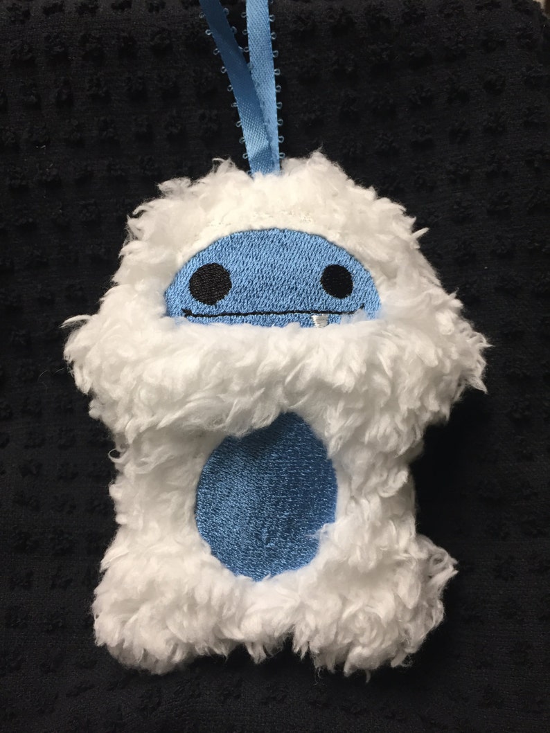 Puede incluir: Adorno de yeti de peluche blanco con cara y vientre azules. El yeti tiene ojos bordados negros y boca cosida. Se adjunta una cinta azul claro para colgarlo. El adorno est&aacute; hecho de material suave y esponjoso.