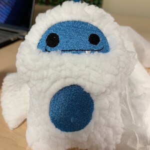 Puede incluir: Un peluche con forma de yeti, con un exterior blanco y esponjoso y una cara azul con ojos negros y una sonrisa cosida. Un gran c&iacute;rculo azul est&aacute; en el cuerpo del yeti. El juguete est&aacute; dise&ntilde;ado para parecerse a un personaje de dibujos animados.