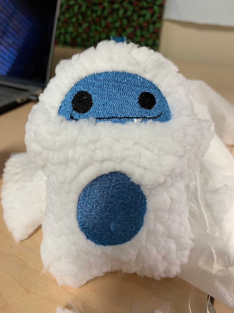 Puede incluir: Un peluche con forma de yeti, con un exterior blanco y esponjoso y una cara azul con ojos negros y una sonrisa cosida. Un gran c&iacute;rculo azul est&aacute; en el cuerpo del yeti. El juguete est&aacute; dise&ntilde;ado para parecerse a un personaje de dibujos animados.