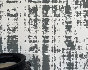 Op de afbeelding: Een close-up van een wit en grijs getextureerd behang met een zwarte kaarsenhouder op de voorgrond.
