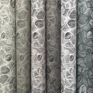 May include: A collection of rolled fabric samples with a repeating abstract pattern. The design features interconnected lines and shapes in shades of gray and white, creating a textured appearance. The rolls are arranged vertically, showcasing the variety of patterns.