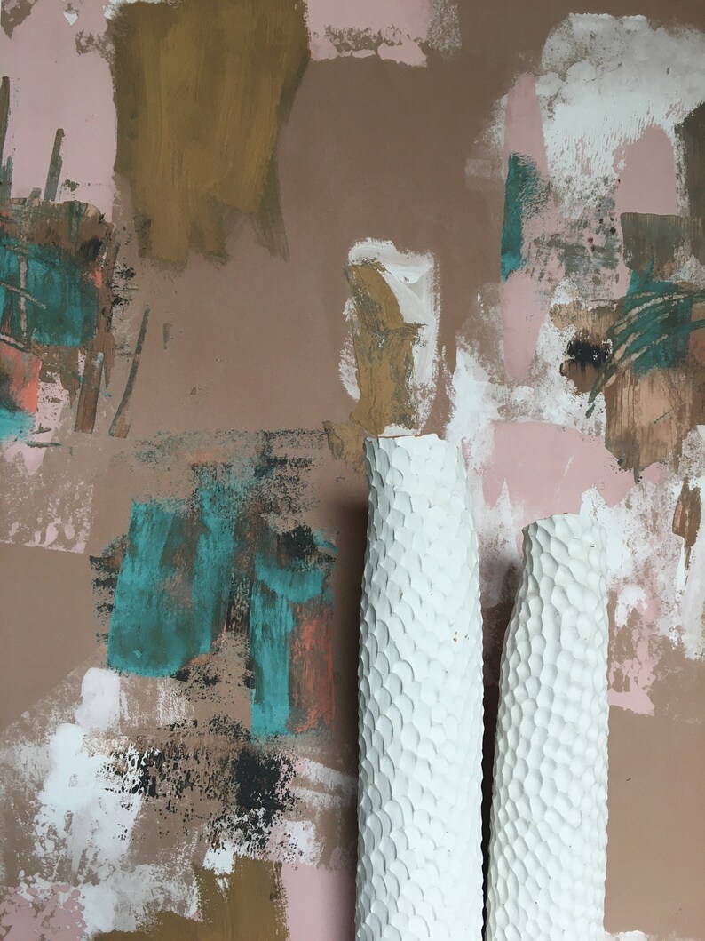 May include: Two white ceramic vases with a textured surface. The vases are in front of a wall with abstract painted designs in shades of brown, pink, teal, and white.