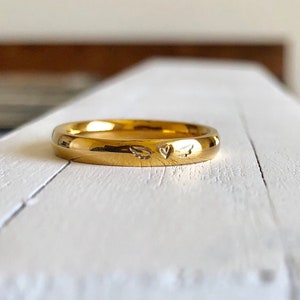 May include: A gold band ring with a small heart and wings engraved on the top.