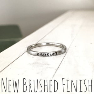 May include: A silver ring with a brushed finish and the name "gabriel" engraved on it.