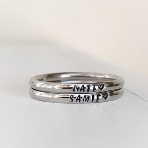 May include: Two silver rings with the names "Nate" and "Samie" engraved on them, each name followed by a small heart symbol.