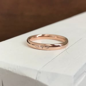 May include: A simple rose gold band ring with a small heart and arrow engraved on the inside.