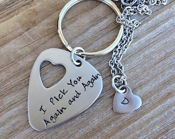 May include: A silver-colored keychain with a guitar pick-shaped pendant featuring a heart-shaped cutout and the inscription "I Pick You Again and Again." A small heart-shaped pendant with the letter "D" hangs from a chain.