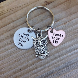 Pode incluir: Chaveiro com um charme de coruja prateada, um charme redondo prateado que diz "owl always love you" e um charme de cora&ccedil;&atilde;o de cobre que diz "love your sis".