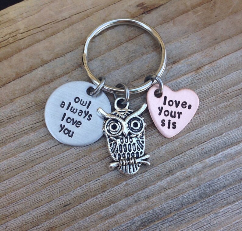 Pode incluir: Chaveiro com um charme de coruja prateada, um charme redondo prateado que diz "owl always love you" e um charme de cora&ccedil;&atilde;o de cobre que diz "love your sis".